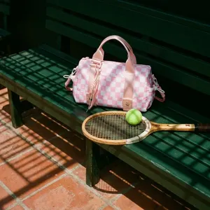 Borsa da viaggio a scacchi rosa su panca verde con attrezzatura da tennis, dettaglio