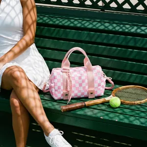 Grande borsa da viaggio a scacchi rosa e bianca su panca verde con set da tennis.