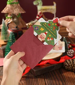 Hand placing a festive Christmas tree card into a red envelope for holiday gifting.
