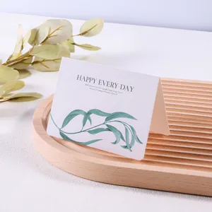 Gedetailleerd zicht op minimalistische bosstijl wenskaart met groen bladmotief op houten tray