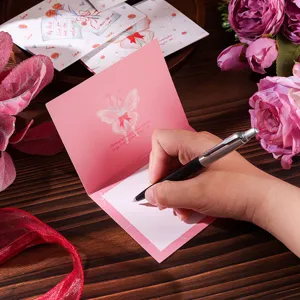 Close-up of hand writing a message on a pink floral butterfly Valentine folding card