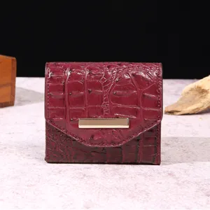 Detalle de cartera vintage granate con relieve de cocodrilo y barra decorativa dorada.