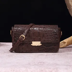Primer plano de bolso bandolera marrón con relieve de cocodrilo y un cierre dorado