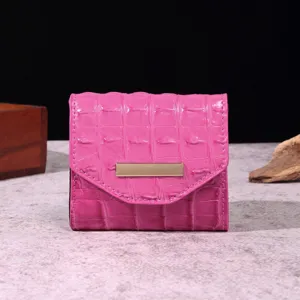 Vista frontal de una cartera rosa con textura de cocodrilo y barra dorada elegante