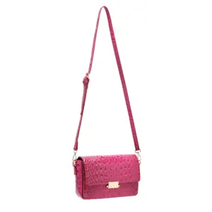 Detalle de bolso bandolera fucsia con grabado de cocodrilo y herrajes dorados