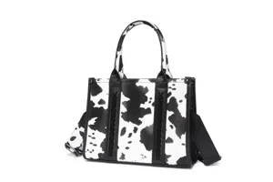Detalle de bolso con estampado de vaca, cordones trenzados negros y correa ancha de hombro