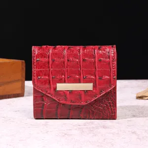 Vista frontal de una cartera roja para mujer con patrón de cocodrilo y adorno de metal dorado.