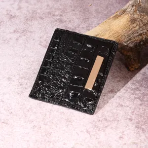 Dettaglio di un porta carte nero con trama a coccodrillo e inserto in metallo dorato.