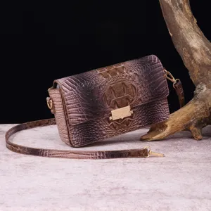 Vista detallada que muestra la textura de cocodrilo en un bolso bandolera de cuero degradado marrón.