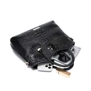 Elegante bolso negro con relieve de cocodrilo muestra capacidad con móvil y gafas.