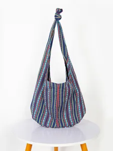 Bolso bandolera vintage de lona con estampado azteca y rayas étnicas en mesa blanca.