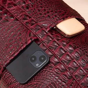 Detalle de bolso burdeos con textura de cocodrilo y bolsillos para el móvil y accesorios