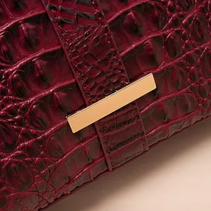 Primer plano de bolso burdeos con grabado de cocodrilo y detalle de metal dorado.