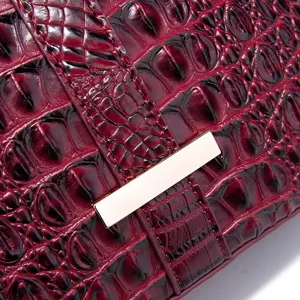 Primer plano de un bolso burdeos con patrón de cocodrilo en relieve y herrajes dorados