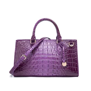 Elegante bolso de mano de piel violeta con relieve de cocodrilo y detalles dorados.