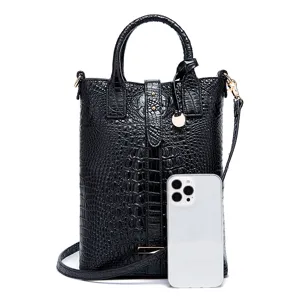 Detalle de bolso negro con patrón de cocodrilo y smartphone para referencia de tamaño