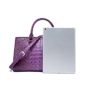 Comparación detallada de tamaño de bolso morado con grabado de cocodrilo y tableta.