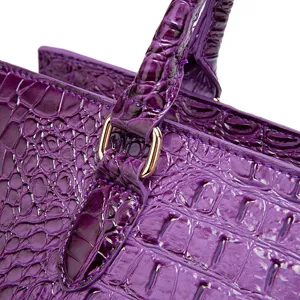 Detalle de bolso morado con relieve de cocodrilo y herrajes dorados.