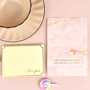 Detalle de tarjeta de felicitación bronceada con patrón de mármol rosa y frases románticas.