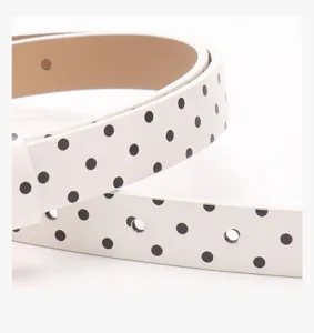 Détail d'une ceinture en cuir blanc à pois noirs montrant les trous et la finition vernie