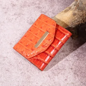Detalle de cartera naranja con patrón de cocodrillo y detalles dorados.