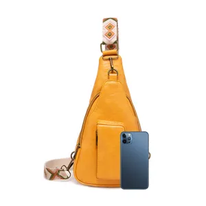 Bolso de pecho bohemio amarillo con correa de colores, mostrado con un móvil para escala.