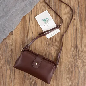 Vintage brown leather frame bag with adjustable strap on a rustic wood background.