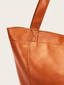 Primer plano de costuras reforzadas y textura de cuero encerado en un bolso tote marrón