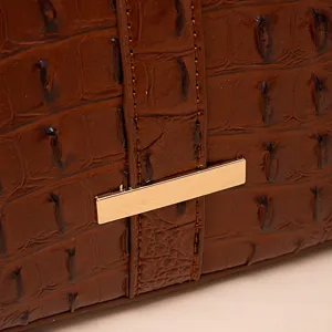 Primer plano de piel grabada de cocodrilo marrón y barra dorada en el bolso de mujer