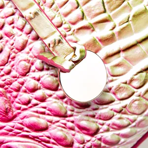 Primer plano de textura de cuero de cocodrilo rosa y herrajes de metal de un bolso vintage.