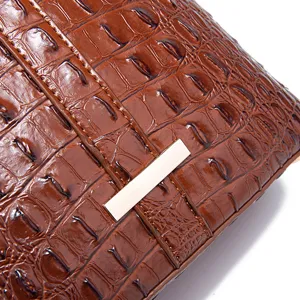 Primer plano del bolso vintage marrón con relieve de cocodrilo y adorno de metal dorado.