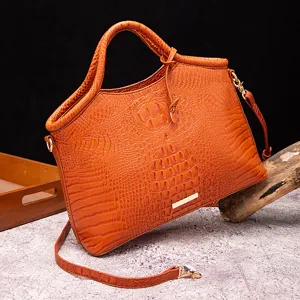 Vista detallada de un bolso naranja con patrón de cocodrilo y elegantes acabados dorados.