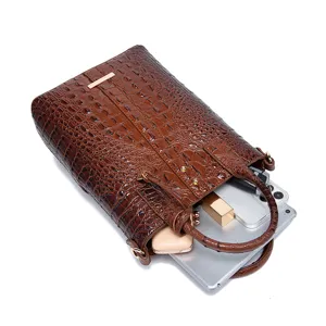 Bolso de mano marrón con relieve de cocodrilo muestra la capacidad para tablet y móvil
