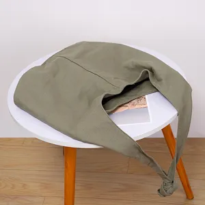 Detalle de bolso bandolera de lona verde oliva con correa anudada en una mesa
