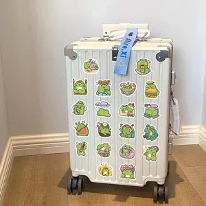 Macro detail of various cute cartoon frog doodle stickers on a white textured suitcase.