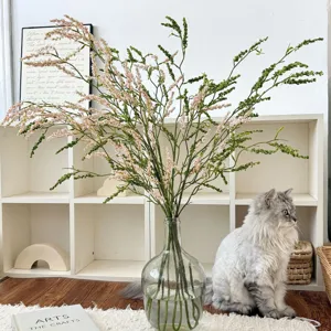 Kunstmatige rijstgrasbloemen in een glazen vaas voor moderne woonkamer decoratie.