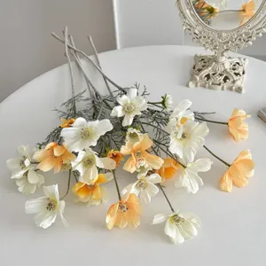 Detail showing white and orange artificial cosmos flowers on a white table
