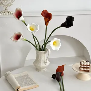 Lis calla en PU multicolores réalistes dans un élégant vase blanc sur une table