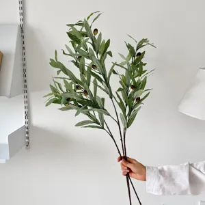 Detailed macro view of artificial olive branches with realistic fruits held by hand.
