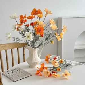 Detail of lifelike orange and white artificial cosmos petals and stems in a white vase