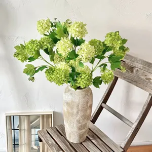 Detailopname van kunstmatige groene sneeuwbalhortensia's in een rustieke vaas met textuur.