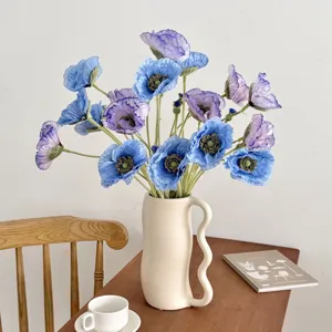 Amapolas artificiales azules de 5 cabezas en un jarrón blanco minimalista en una mesa