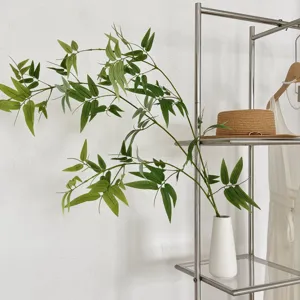 Single artificial bamboo leaf branch in a white minimalist vase for Zen home decor