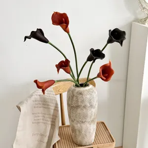 Gros plan de lys calla en PU réalistes dans un vase en pierre sur une chaise en bois.
