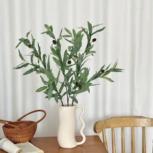 Close-up of realistic artificial olive branch with fruits in a stylish white vase