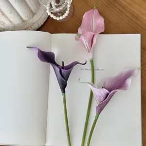Primer plano de tres calas artificiales en tonos morados y rosas sobre un libro.