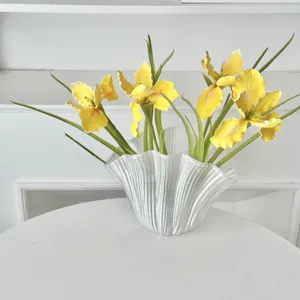 Vibrant yellow artificial iris flowers in a white textured glass vase for home decor.