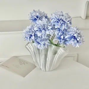 Detailed close-up of artificial blue dahlia flowers in a textured white glass vase
