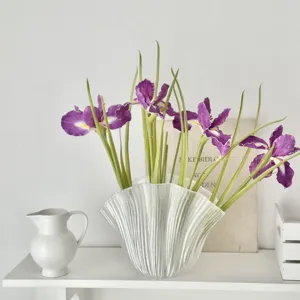 Close-up of purple artificial iris flowers in a shell-shaped glass vase on shelf