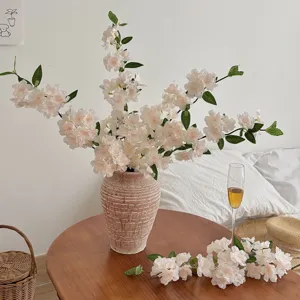 Close-up of elegant artificial cherry blossom branches in a rustic textured ceramic vase.